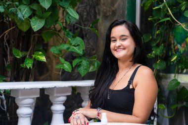 Güzel, siyah saçlı bir kadın yeşil yapraklı, sakince oturuyor. Seyahat eden kişi.