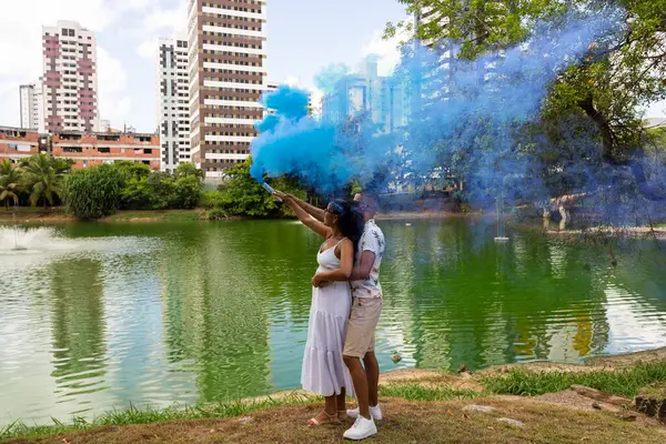 Happy couple having a gender reveal party. blue smoke grenade outdoors. It's a boy. Gender reveal party concept. Couple in love