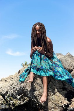 Mavi elbiseli ve örgülü saçlı güzel bir kadının portresi kumsalın kayalarında mavi gökyüzüne karşı oturuyordu..