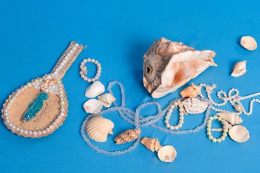 Mavi stüdyo zeminine dağılmış birkaç deniz kabuğu, kolye ve ayna. Iemanja 'ya haraç.