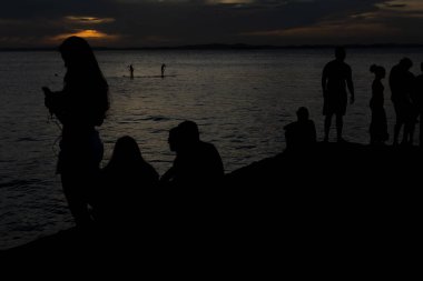 Tanımlanamayan insanların silueti koyu bulutlu ve sarı renkli güneşli dramatik günbatımının tadını çıkarıyor. Bahia, Salvador şehri..