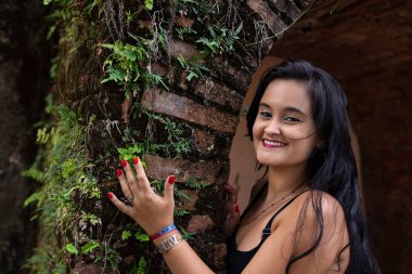 Güzel siyah saçlı kadın kameraya bakan tuğlalardan yapılmış antik bir duvara dokunuyor. Keyifli bir yolculukta.