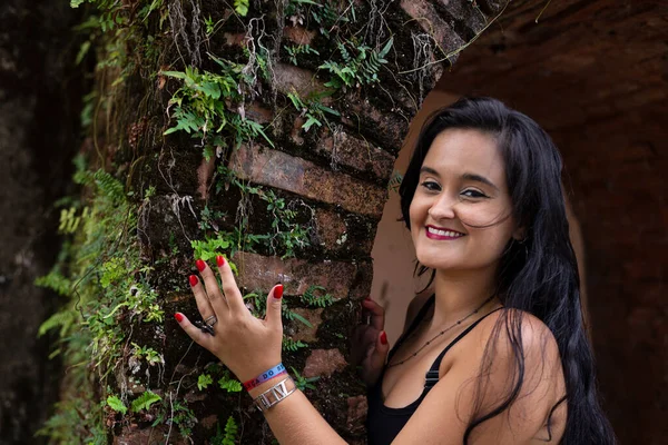 Güzel siyah saçlı kadın kameraya bakan tuğlalardan yapılmış antik bir duvara dokunuyor. Keyifli bir yolculukta.