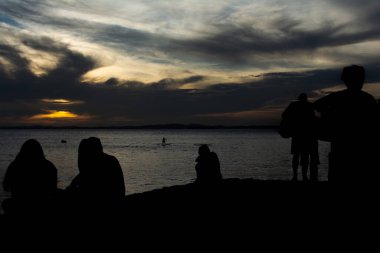 Tanımlanamayan insanların silueti koyu bulutlu ve sarı renkli güneşli dramatik günbatımının tadını çıkarıyor. Bahia, Salvador şehri..