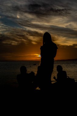 Tanımlanamayan insanların silueti koyu bulutlu ve sarı renkli güneşli dramatik günbatımının tadını çıkarıyor. Bahia, Salvador şehri..