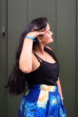 Yeşil kapıya karşı fotoğraf için poz veren siyah saçlı genç bir kadın. Seyahat eden mutlu kişi.