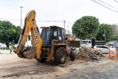 Salvador, Bahia, Brezilya - 05 Ocak 2024: Bahia 'nın Salvador kentindeki ticari bölgede Conceicao da Praia caddesindeki yeniden inşa çalışmasında taşları taşıyan Backhoe traktörü.
