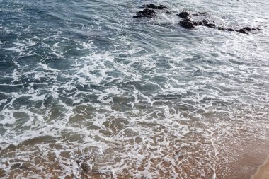 Küçük köpüklü dalgalarla dolu bir sahil kenarında. Güneşli gün, sakin deniz suyu.