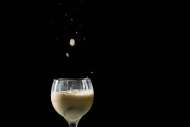 Şarap bardağına düşen süt damlaları. Siyah arkaplanda izole.