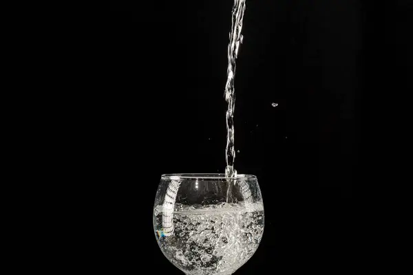 Water falling from above into a wine glass. Isolated on black background.