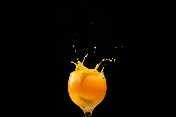 Splash in a glass goblet with orange juice inside. Isolated on black background.