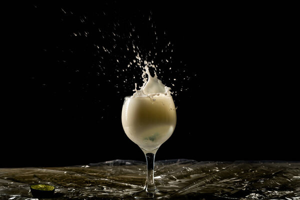 Splash in a glass bowl with milk inside. Drops in the air. Isolated on black background.