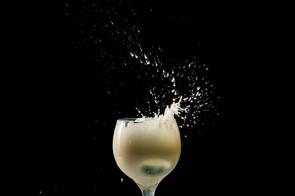 Splash in a glass cup with milk inside. Drops flying in different directions. Isolated on black background.