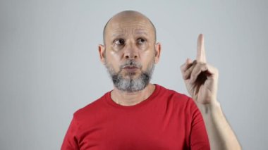 Kel sakallı adam iki elini de yukarı kaldırdı. Gösterdiğine çok güveniyor. Gri arkaplanda izole.