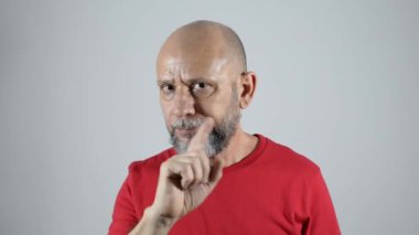 Kel sakallı adam sağ eliyle negatif işaret veriyor. Gri arkaplanda izole edilmiş kırmızı renkli gömlekli..