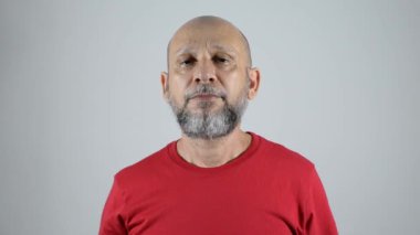 Kırmızı tişörtlü kel sakallı adam sağ tarafa baş parmak işareti yapıyor. Gri arkaplanda izole.