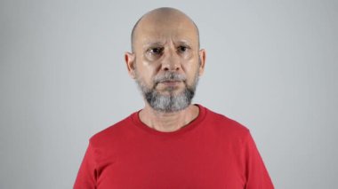 Kırmızı tişörtlü, kel ve sakallı sakin ve sakin bir adam elleriyle alkışlıyor. Gri arkaplanda izole.