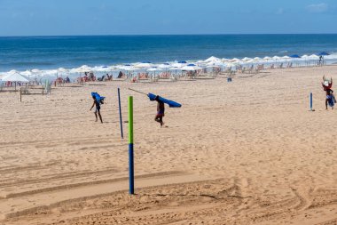 Salvador, Bahia, Brezilya - 16 Mart 2019: Salvador, Bahia 'daki Jardim de Ala plajında sırtlarında şemsiyeler taşıyan sahil işçilerinin görüntüsü.