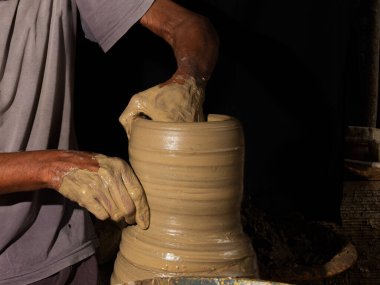 Seramik tencereyi şekillendiren bir zanaatkarın ellerine yakın çekim. Siyah arkaplanda izole