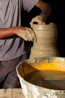 Seramik tencereyi şekillendiren bir zanaatkarın ellerine yakın çekim. Siyah arkaplanda izole