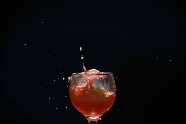 Splashes in a glass cup with guava juice inside. Isolated on dark background.