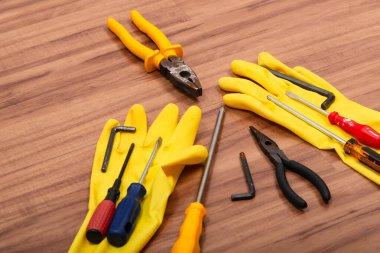 Bir çift temizlik eldiveni, pense, tornavida, ingiliz anahtarı ve ahşap arka planda izole edilmiş diğer aletler..