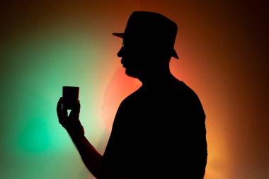 Şapkalı bir adam elinde renkli arka planda bir fincan kahve tutuyor..