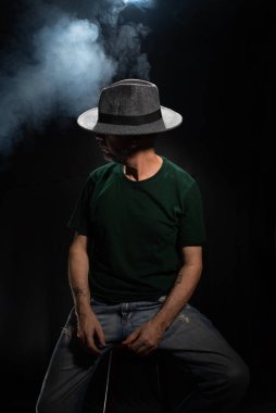 Yüzünü örten şapka giyen gizemli, sakallı bir adam. Stüdyo portresi. Yapay dumanlı koyu arkaplan.