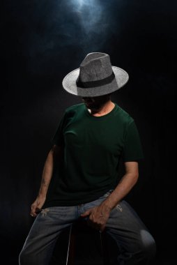 Yüzünü örten şapka giyen gizemli, sakallı bir adam. Stüdyo portresi. Yapay dumanlı koyu arkaplan.
