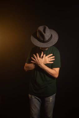 Fotoğraf için poz veren şapkalı gizemli adam. Stüdyo portresi. Yapay dumanlı kırmızı koyu arkaplan.