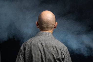 Bald middle-aged man with his back to the camera. Isolated on studio artificial smoke filled background. clipart