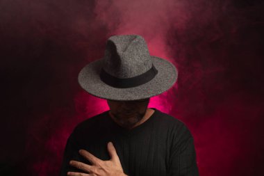 Gizemli, orta yaşlı, gri şapkalı bir adam. Kırmızı gül rengi ile doldurulmuş yapay dumanla izole edilmiş..