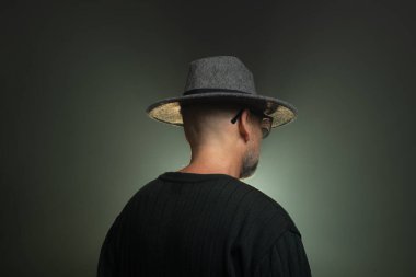 Kafasına şapka takmış gizemli, orta yaşlı bir adam. Stüdyoda fotoğraf. Yapay dumanlı stüdyo arkaplanı.