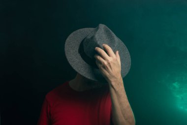 Sakallı adam şapka takıyor ve fotoğraf için poz veriyor. Stüdyoda portre. Yapay dumanlı yeşil arkaplan.