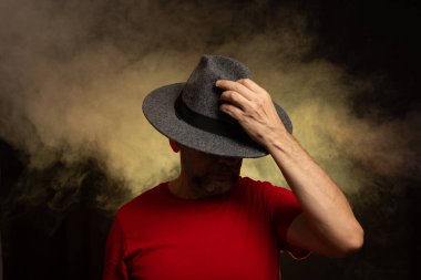 Sakallı adam şapka takıyor ve fotoğraf için poz veriyor. Stüdyoda portre. Yapay dumanlı sarı arkaplan.