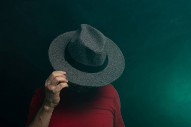 Sakallı adam şapka takıyor ve fotoğraf için poz veriyor. Stüdyoda portre. Yapay dumanlı yeşil arkaplan.