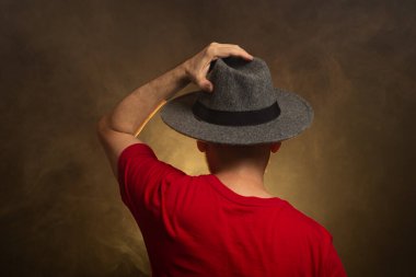 Sırtı kameraya dönük, şapkalı ve fotoğraf için poz veren orta yaşlı sakallı bir adam. Yapay dumanlı renkli stüdyo arkaplanı.