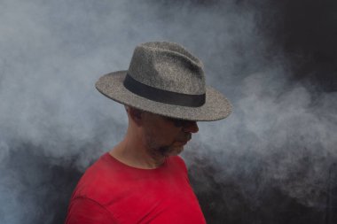 Gözlüklü, şapka takan sakallı adam. Stüdyo portresi. Yapay dumanlı gri arkaplan.