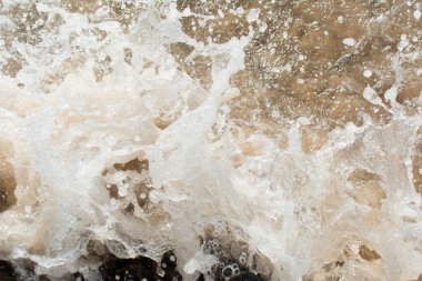 Plaj suyu karanlık kayalara çarpıyor. Korunmuş doğa.