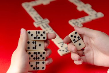 Domino oyuncularının elleri dikdörtgen sayı bloklarını tutuyor. Masa oyunu. Kırmızı arkaplan.