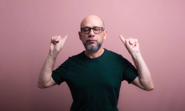 Parmağıyla işaret eden reçeteli gözlüklü kel bir adam. Somon renkli arka planda izole edilmiş.