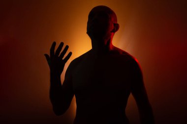 Silüetli, hareketsiz ve üstsüz bir adam fotoğraf için poz veriyor. Turuncu arkaplanda izole.