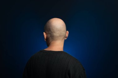 Bearded, bald middle-aged man with his back to the camera. Photo in studio. Blue studio background with artificial smoke. clipart