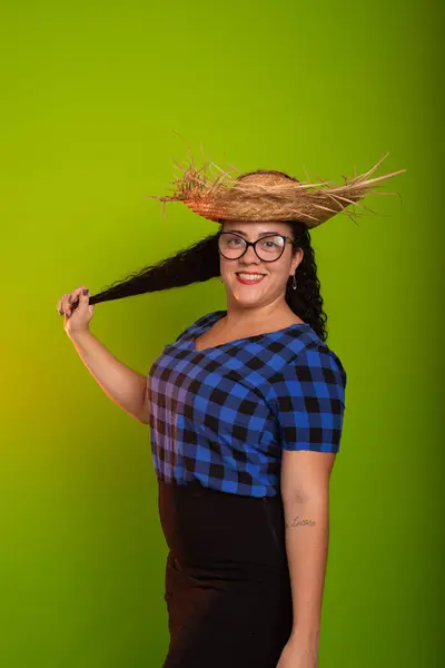 stock image Young woman dressed in character for the Sao Joao festival wearing a straw hat and prescription glasses holding her hair. Isolated on green background.