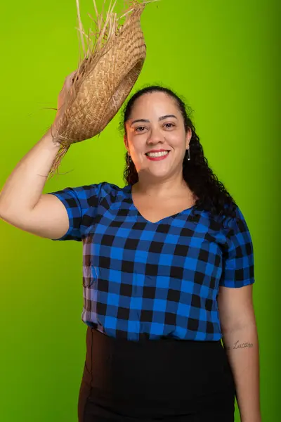 stock image Young woman dressed in character for the Sao Joao festival, placing a straw hat on her head. Isolated on green background.