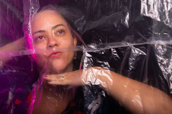 Stock image Beautiful woman behind transparent plastic posing. Photo in studio. Suffocation concept. Isolated on black background.