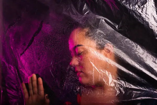 stock image Beautiful woman touching her hands on a transparent plastic. Isolated on black background.