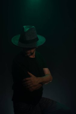 Kameraya poz veren gizemli, sakallı adam. Stüdyo portresi. Yapay dumanlı koyu yeşil arkaplan.