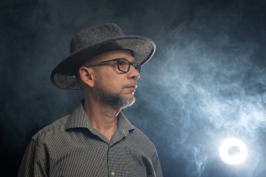 Middle-aged man with a beard wearing a hat and posing for the camera. Isolated on smoke-filled background. clipart