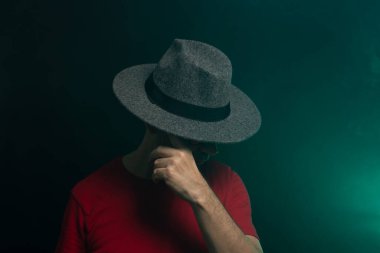 Sakallı adam şapka takıyor ve fotoğraf için poz veriyor. Stüdyoda portre. Yapay dumanlı yeşil arkaplan.
